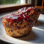Two perfectly baked mini meatloaf portions topped with a shiny red glaze, sitting on a white plate.