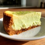 A close-up of a perfect slice of key lime cheesecake on a white plate, topped with lime zest.