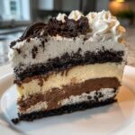 A tall slice of layered ice cream cake featuring vanilla and chocolate ice cream layers, Oreo crusts, and whipped cream topping.