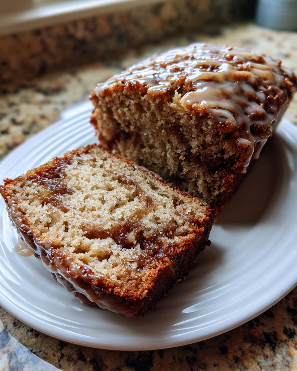 A slice of moist apple bread with a visible cinnamon swirl, topped with a sweet glaze, resting next to the main loaf.