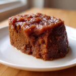 A close-up of a moist, dark cake generously topped with thick, glossy pear butter on a white plate.