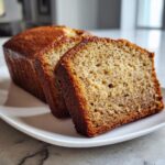 Close-up of three slices of moist greek yogurt banana bread with a dark golden crust, served on a white plate.