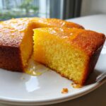 Close-up of a vibrant yellow slice cut from an olive oil cake, drizzled with a shiny glaze.