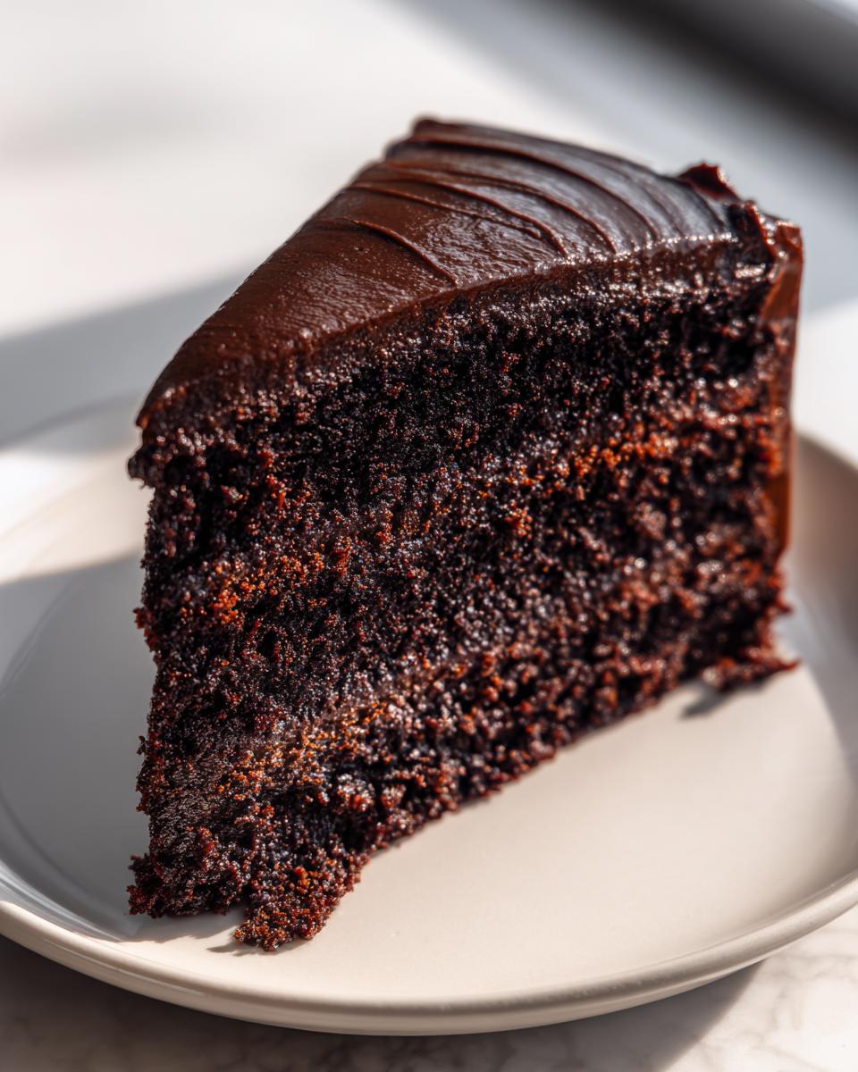 Close-up of a rich, dark slice of chocolate cake recipe with glossy frosting.
