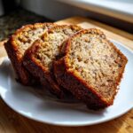 Three moist slices of golden brown sourdough banana bread served on a white plate, ready to eat.