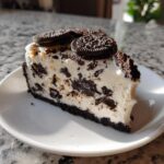 A generous slice of no bake oreo pie with cream filling and chocolate cookie chunks, topped with whole Oreos.