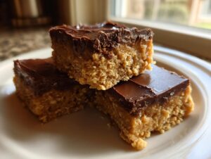 Three stacked no-bake peanut butter bars featuring a thick, textured base and a smooth chocolate topping.