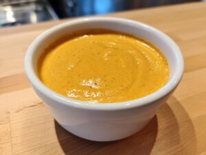 A close-up shot of creamy, orange-yellow beer cheese dip served in a small white bowl on a wooden counter.