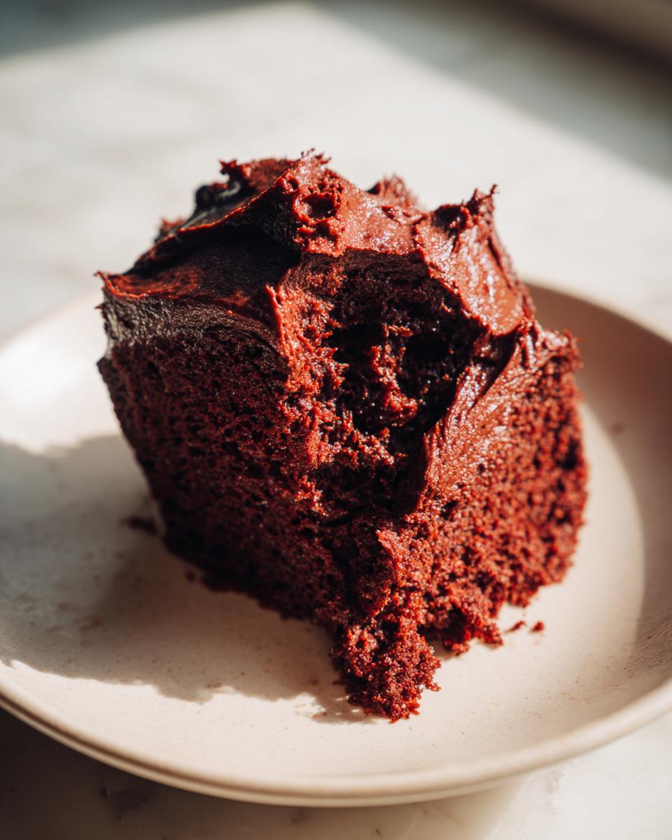 Close-up of a dark, rich slice of cake generously topped with thick chocolate frosting.