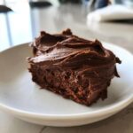 Close-up of a rich, dark chocolate cake slice topped generously with creamy chocolate frosting.