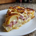 A thick slice of scalloped potatoes and ham, layered with creamy sauce and topped with browned cheese.