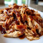 Close-up of tender, shredded crockpot teriyaki chicken generously coated in a thick, glossy teriyaki sauce.