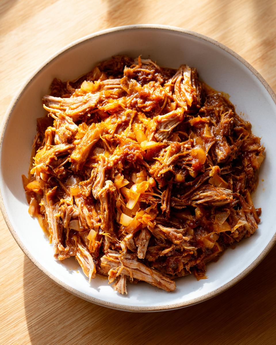 Close-up of tender, shredded pork and sauerkraut mixture served in a light ceramic bowl.
