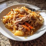 A close-up of shredded pork and sauerkraut mixed with carrots and potatoes served on a white plate.