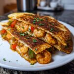 Two halves of a perfectly grilled shrimp quesadilla overflowing with seasoned shrimp, peppers, and melted cheese.
