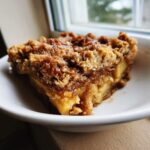 Close-up of a warm slice of apple crisp recipe showing soft baked apples and a thick, golden brown, crunchy oat topping.