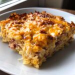 A square slice of homemade reuben bake featuring layers of corned beef and sauerkraut topped with melted, browned cheddar cheese.