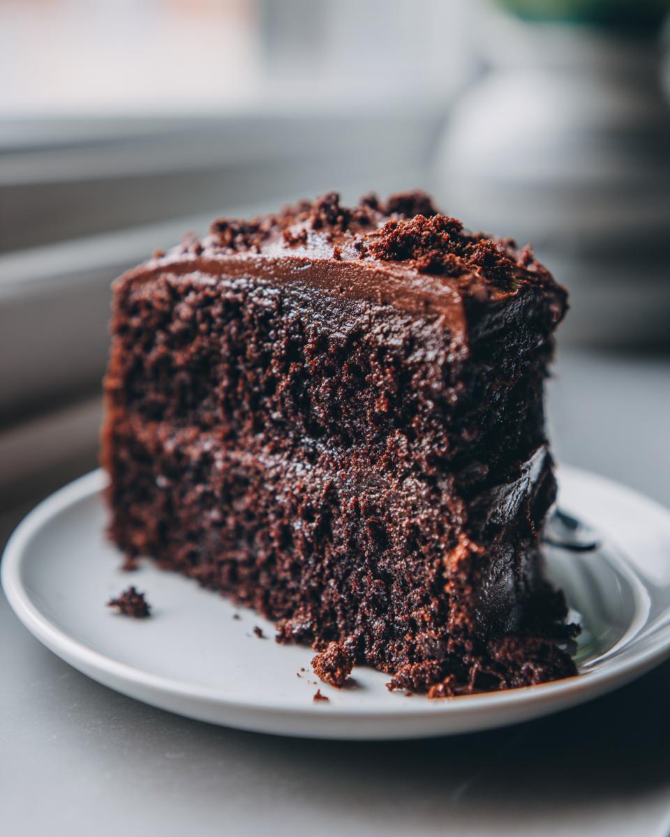 Close-up of a rich, dark slice of chocolate cake recipe served on a white plate.