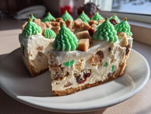 A slice cut from a rich christmas tree cheesecake, topped with green frosting trees and caramel pieces.