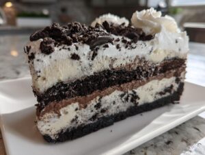 Close-up of a rich slice of layered ice cream cake featuring dark chocolate cookie crust, vanilla and chocolate ice cream layers, topped with whipped cream and cookie crumbles.