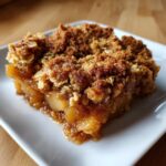 Close-up of a moist slice of pear crisp showing tender fruit filling and a thick, crunchy oat topping.