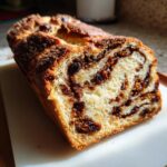 A close-up view of a freshly baked loaf of raisin bread, showing the soft interior swirled with cinnamon and plump raisins.