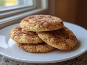 A stack of four soft, chewy snickerdoodle cookies coated in cinnamon sugar, resting on a white plate.