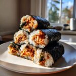 A stack of six cut pieces of spicy tuna kimbap, showing the bright orange tuna filling surrounded by white rice and dark seaweed.