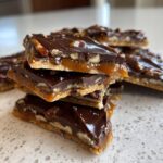 A stack of rich Pecan Pie Bark squares showing layers of crust, gooey caramel, pecans, and a dark chocolate topping.