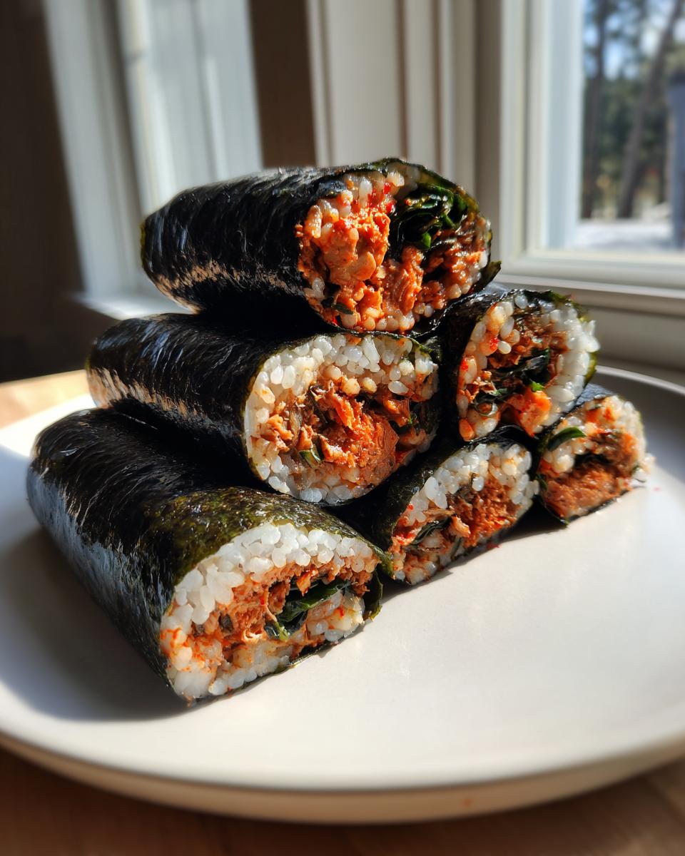 A stack of freshly cut tuna kimbap rolls showing the white rice and spicy red tuna filling inside the dark seaweed wrapper.