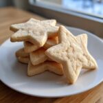 A stack of star-shaped soft sugar cookies sprinkled with coarse sugar, resting on a white plate.