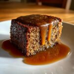 A square slice of rich, dark sticky toffee pudding recipe covered in thick toffee sauce dripping down the side.