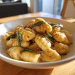 A close-up of homemade sweet potato gnocchi tossed in a light sauce and garnished with crispy sage leaves.
