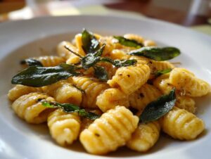 A close-up of golden sweet potato gnocchi tossed in butter sauce and topped with crispy fried sage leaves.