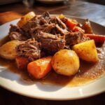 Close-up of tender shredded pot roast served with chunks of carrots and potatoes in rich brown gravy.