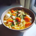 Close-up of a bowl of rich turkey noodle soup featuring shredded turkey, bright orange carrots, egg noodles, and fresh parsley.