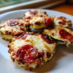 Close-up of several baked zucchini pizza bites topped with melted mozzarella cheese and pepperoni slices.