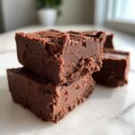 Close-up of two stacked, rich, dark chocolate squares from the 3-ingredient fudge recipe on a white marble surface.