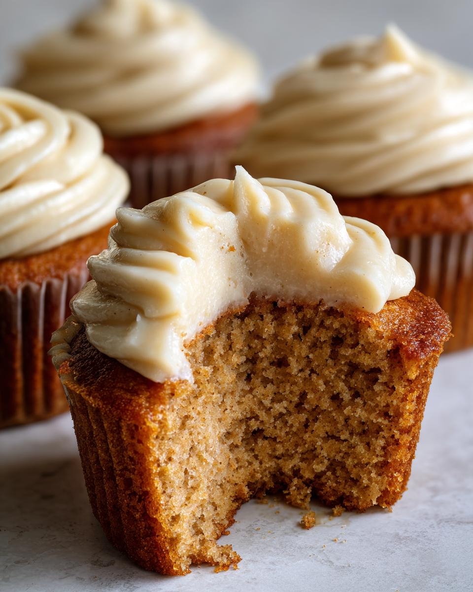 Close-up of a banana cupcake with a bite taken out, revealing the moist crumb and thick cream cheese frosting.