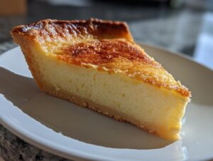 A perfect slice of amazing buttermilk pie showing a creamy yellow filling and a deeply browned, caramelized top crust.