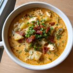 A close-up overhead view of a hearty bowl of amazing cheeseburger soup, topped with crumbled bacon and fresh green onions.