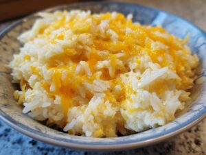 Close-up of amazing cheesy rice topped with melted cheddar cheese served in a decorative blue and white bowl.
