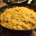 A close-up view of homemade cheesy rice mixed with melted cheddar cheese in a dark skillet.
