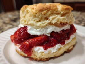 Close-up of a fluffy biscuit split and filled with whipped cream and macerated strawberries for strawberry shortcake.