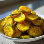 A white bowl piled high with glistening, yellow-green slices of homemade bread and butter pickle.