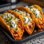 Three crispy buffalo chicken tacos loaded with orange shredded chicken, melted cheddar, blue cheese crumbles, and sour cream.