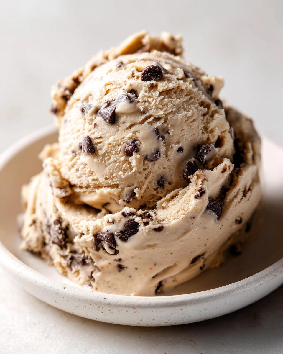 A close-up of a scoop of creamy chocolate chip cookie dough ice cream in a speckled white bowl.