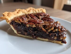 A close-up of a rich, gooey slice of chocolate pecan pie topped with whole pecans, sitting on a white plate.