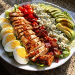 A beautifully arranged Cobb salad featuring sliced grilled chicken, hard-boiled eggs, bacon, avocado, blue cheese, and tomatoes.