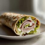 Close-up of a delicious cottage cheese wrap sliced to show layers of ham, cottage cheese, and lettuce.